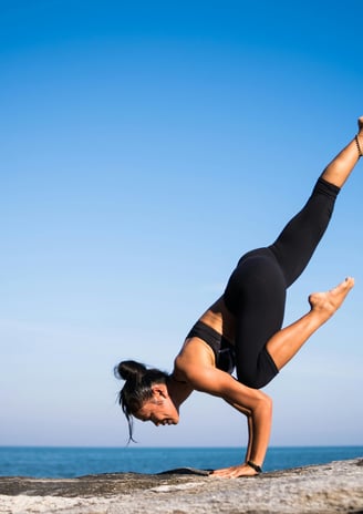 er is een vrouw te zien die yoga uitoefent met op de achtergrond de zee en blauwe lucht