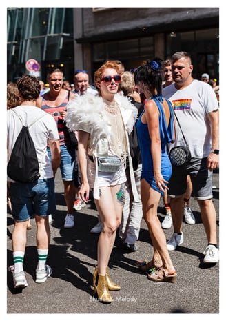 Eine Frau in einer Menschenmenge trägt eine Sonnenbrille und einen Federmantel.