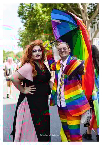Eine Drag Queen und ein Mann mit Regenbogenanzug, Hut und Regenschirm bei der Christopher Street Day