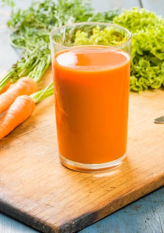 a glass of carrot juice on a cutting board