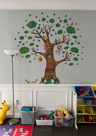 Photo of daycare room where children play. Large tree sticker on wall.