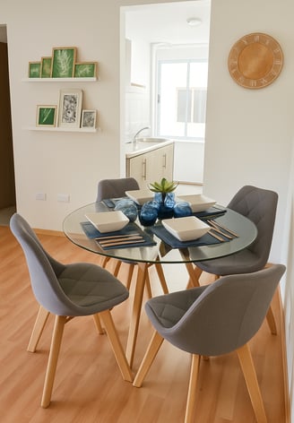 Comedor de departamento muestra con mesa redonda de cristal, sillas tapizadas en gris, decoración
