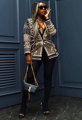 Efia Odo in a glittering designer shirt with black leggings and holding a designer bag.