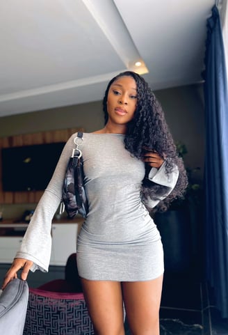 Efia Odo in a gray overall dress with a black handbag.