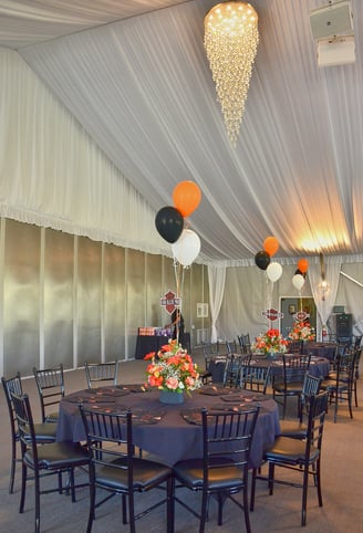 a large tented room with decorated round tables with balloons and chairs 