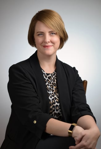 a woman in a black jacket and leopard print top sitting in front of a white background