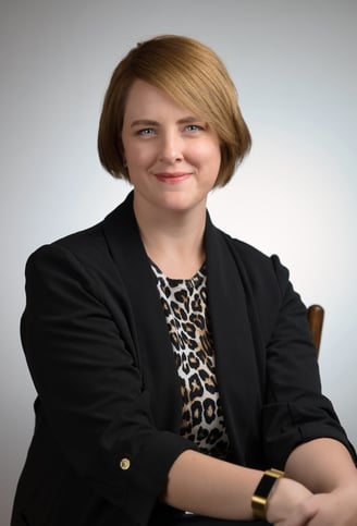 a woman in a black jacket and leopard print top sitting in front of a white background
