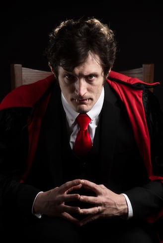 a man in a vampire suit with vampire teeth out and tie with a red tie  