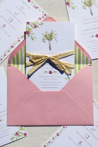 close up of invitation with pomegranate tree inside of pink envelope with stripped green lining