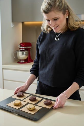 Olivia, Chief Cookie Officer, smiles down at a tray of frozen cookie dough pucks ready for the oven.
