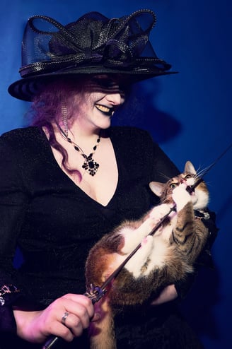 a woman in a black hat holding a cat which is biting a sword