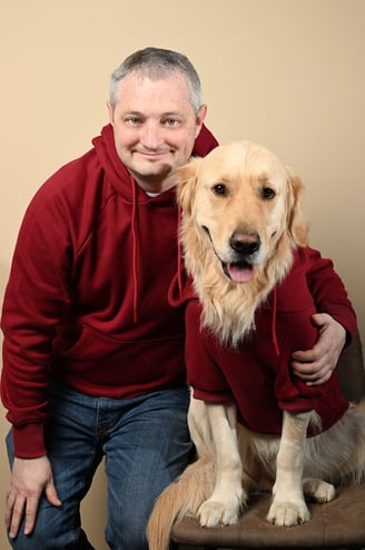 a man in a red hoodie and a golden retriever in a red sweater posing next to each other