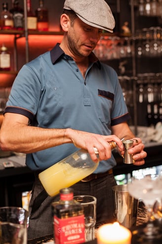 Ein Barkeeper mit Mütze bei der Zubereitung eines Cocktails im Ratzeputz.