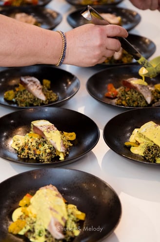 Der Koch gießt eine gelbe Soße über ein Hauptgericht mit Fisch und Quinoa.