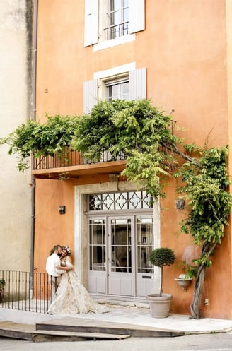 Wide shot of couple in front of ochre building with climbing vine — kiss on the cheek, fine art