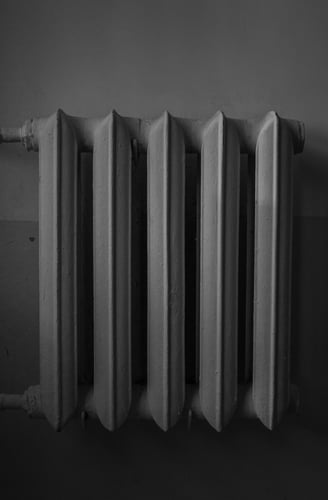 Monochrome image of a cast iron radiator against a wall.