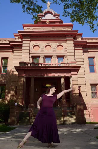 a woman in a purple dress is dancing in front of a historical building