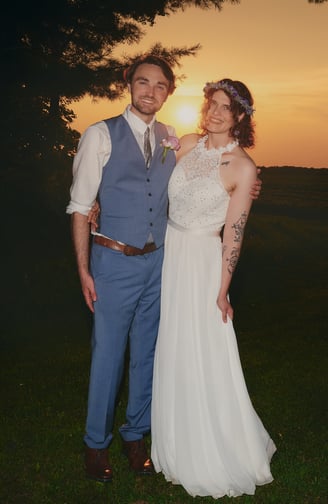 a bride and a groom standing in front of a sunset