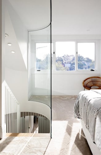 Modern attic bedroom featuring a custom-made curved glass wall panel, blending architectural design