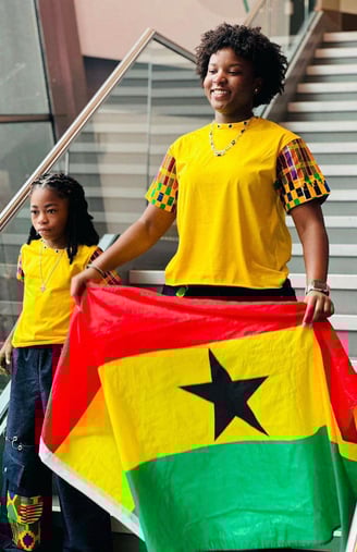 Afronita and Abigail in matching African prints holding a Ghana flag.