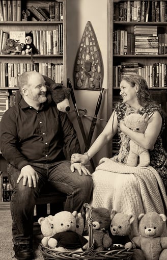 a man and a woman sitting on a chair holding a teddy bear in a library room