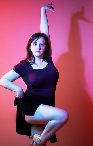 a woman in a black dress and heels is posing as a dancer in front of pink background