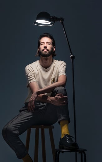 un homme assis sur un tabouret avec une lampe au dessus de lui 