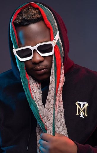 Medikal in a wine sweater wearing dark sunglasses.