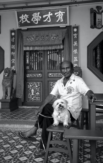 An Indian man and his dog sit outside a temple in Penang by photographer Peter Pickering