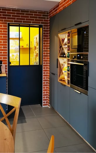 Cuisine vert foncé avec portes anti trace de doigts. Porte cellier style atelier, mur en briques.