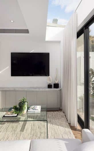 TV area with skylight, soft curtains, wool rug, and glass coffee table in modern living space