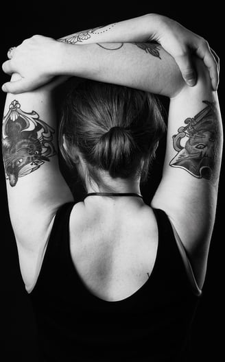a woman showing her back with cat tattoos on her arms which are stretching around her head