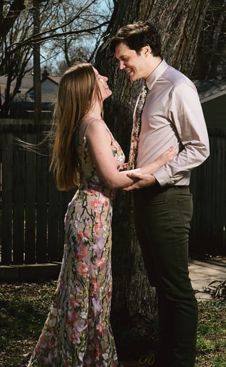 a man and woman facing each other and standing in front of a tree
