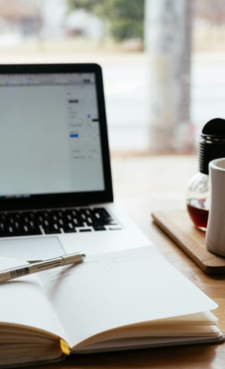 a laptop computer and a notebook with a pen and a cup of coffee