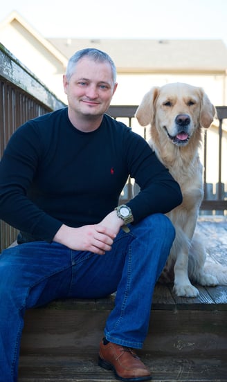 a man sitting on a wooden deck next to his pet the Golden Retriever
