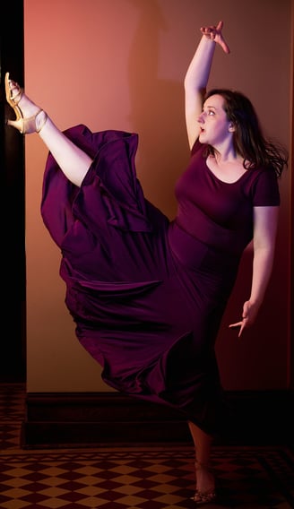 a woman in a purple dress with one leg up dancing in a latin dance style