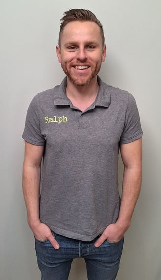 een man in een grijs shirt en broek die voor een muur staat