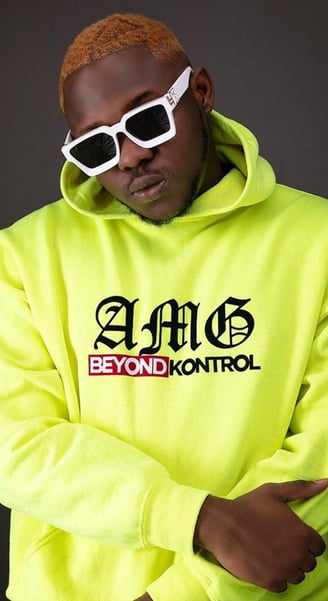 Medikal in a lemon customized AMG Beyond Kontrol sweater in black sunglasses.