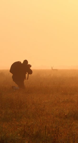 Photographer kneeling in golden morning light capturing wildlife in the African bushveld