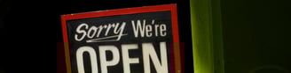 A sign reading "Sorry, We're Open" in the window of lime green Amsterdam cafe.