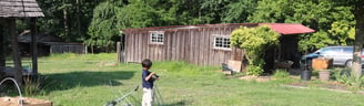 A barn structure in a field with a boy. 