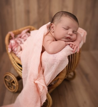 Photo de nouveau né  qui dort dans une petite poussette en rotin, un instant d'émotion et de douceur