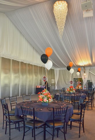 a large tented room with decorated round tables with balloons and chairs 