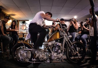 man kickstarting his motorcycle in a bar crowded with people