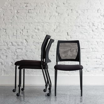 Stacked and upright V137 chairs against a white brick wall, front and side view