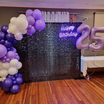 Black shimmer wall with purple garland and neon for Jamila's 25th birthday in Cleveland.