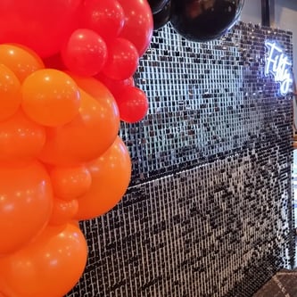 Black shimmer wall with red, orange and black balloons with fifty neon for Shanes birthday.