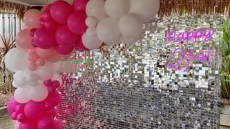 Silver shimmer wall with pink and white balloon garland and happy 21st neon sign.
