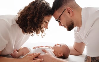 photo de bébé avec ses parents au dessus de lui et les regarde