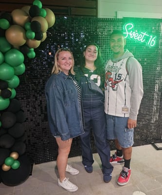 Ashlee with her daughter and husband posing in front of the black shimmer wall and green Sweet 16 neon sign Brisbane
